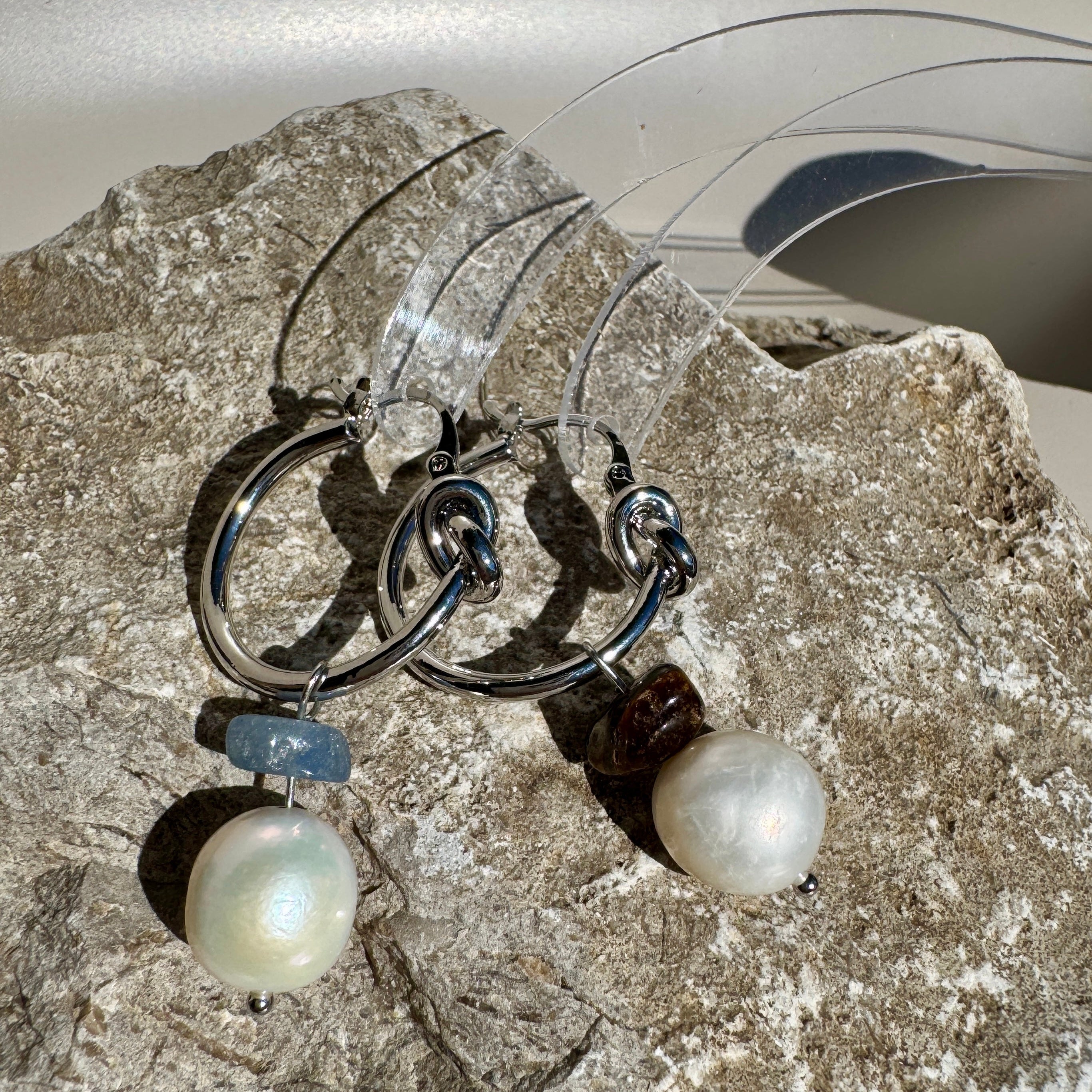 Pair of earrings with pearls and blue stones on a stone surface